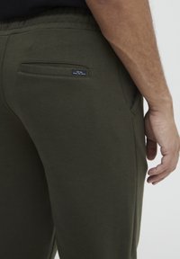 Olivegrüne Baumwoll-Joggings mit einer Gesäßtasche mit einem schwarzen Etikett, elastischem Bund und einer schmalen Passform für Komfort und Vielseitigkeit.