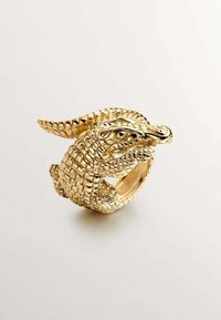 Anillo en forma de cocodrilo de oro que presenta escalas detalladas y un interior suave. El diseño captura la cabeza y la cola del cocodrilo en una pose dinámica.