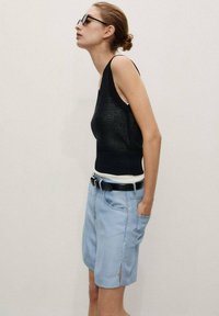 Un débardeur en tricot noir superposé à une chemise blanche, associé à un short bleu clair à hauteur de genou avec des fentes et une ceinture noire.