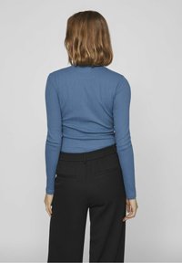 Blusa ajustada de manga larga en azul con un patrón texturizado, combinada con pantalones sueltos negros con cintura elástica y dos bolsillos.