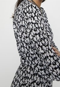 Robe à motifs noir et blanc avec des manches longues, dotée d'une taille froncée et d'un design de tissu texturé. Silhouette minimaliste avec des motifs floraux.