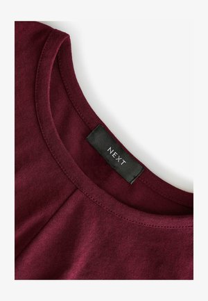 Bordeaux katoen top met een ronde halslijn, subtiele plooidetails en een zwart label met "NEXT" aan de binnenkant van de kraag.