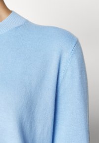 Maglione lavorato a maglia di colore azzurro chiaro con una texture morbida, scollo rotondo e design delle spalle senza cuciture. Il materiale sembra leggero e traspirante.