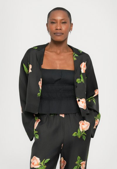 Jachetă neagră cu imprimeu floral, având desene cu trandafiri și frunze, asociată cu un top negru plisat. Material neted și croială lejeră pe toată lungimea.