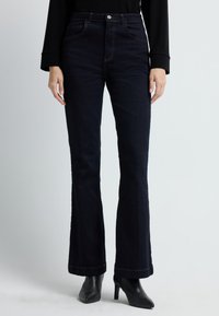 Tummat denimfarkut ovat leveälahkeiset, korkealla vyötäröllä, viidellä taskulla ja niissä on kontrastina oranssia tikkausta. Kangas näyttää sileältä ja siinä on hieman kiiltoa.