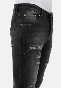 Zwarte denim jeans met een slim fit, voorzien van versleten plekken, rafelige randen en zilverkleurige hardware op de zakken en de tailleband.