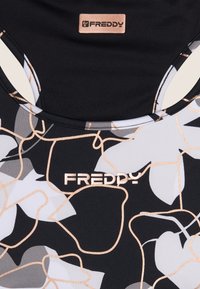 Svart atletisk linne med blommönster i grått och kräm, med en glänsande guldig kant och en liten Freddy-logotagg.