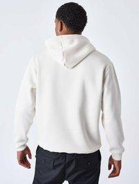 Hoodie blanc avec une capuche à cordon de serrage, des poignets côtelés et un tissu texturé. Pantalons noirs visibles à la taille, montrant des poches.