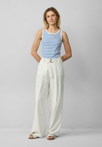 Gestreept tanktop in blauw en wit, gecombineerd met hooggetailleerde crèmekleurige broeken met een riem en gesp. Sandalen maken de outfit compleet.