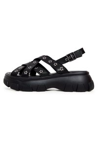 Zwarte sandalen met stervormige zilveren studs, met kruisbanden en een gesp aan de achterkant. Dikke, gestructureerde zool voor extra grip.