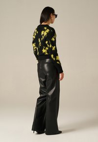 Pull en tie-dye noir et jaune avec une finition texturée, associé à un pantalon en cuir noir taille haute et des escarpins à talons aiguilles.