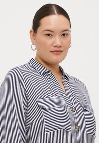 Chemise à boutons rayée en navy et blanc, présentant un col, deux poches poitrine et un tissu texturé.