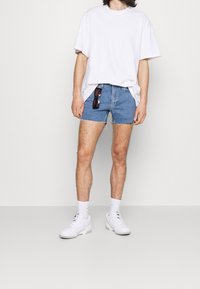 Ljusblå denimshorts med fransade kanter, kombinerat med en överdimensionerad vit t-shirt. Bärs tillsammans med vita sportskor och vita strumpor.