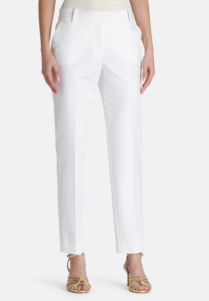 Pantalon blanc sur mesure en tissu lisse, coupe droite, avec poches latérales discrètes, associé à des talons dorés à lanières.