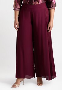 Pantaloni larghi bordeaux con una trama liscia. Presentano pince sui lati e una vita alta, abbinati a sandali beige con tacco.