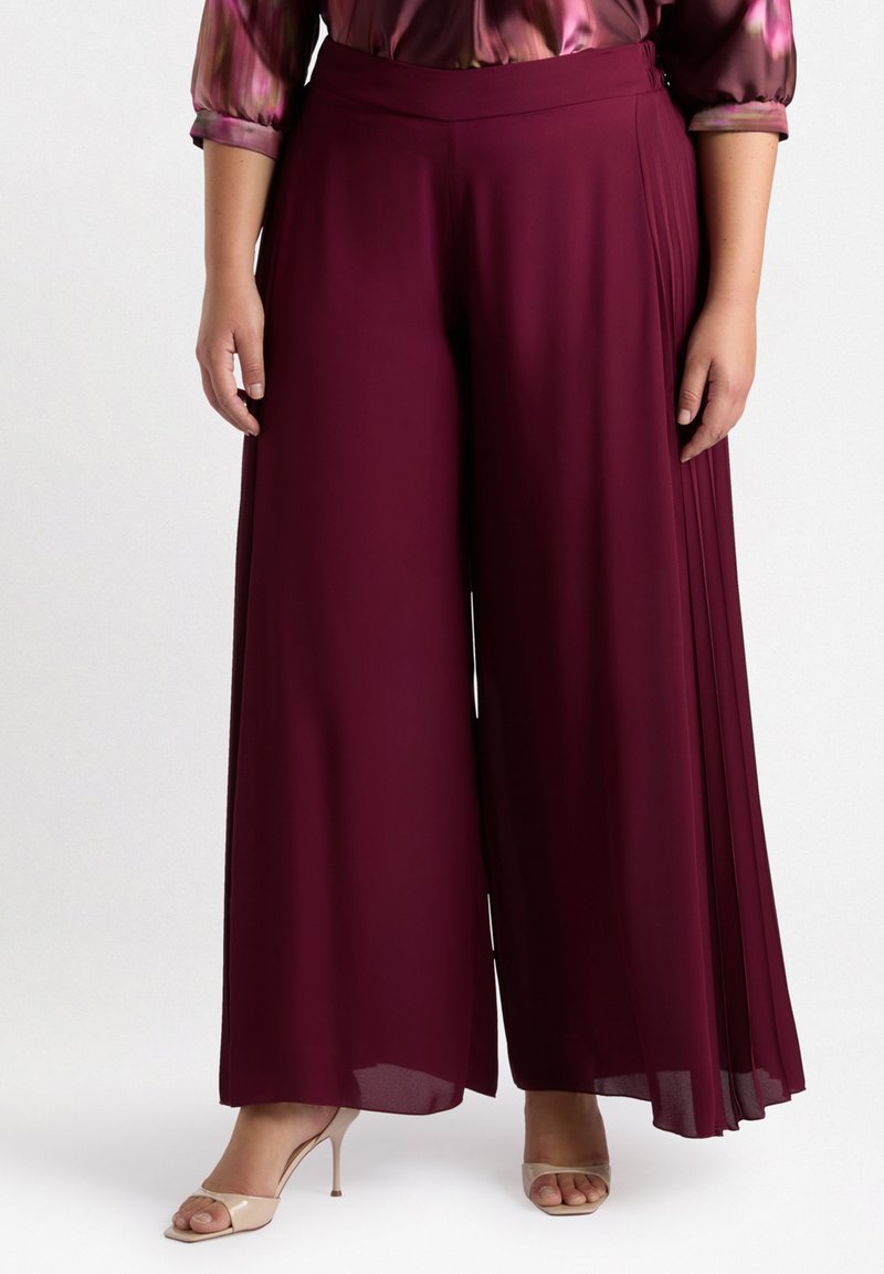 Pantaloni larghi bordeaux con una trama liscia. Presentano pince sui lati e una vita alta, abbinati a sandali beige con tacco.