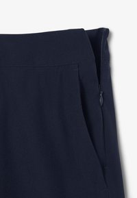 Pantalones azul marino con una textura suave, que cuentan con un bolsillo lateral con cremallera y costuras limpias a lo largo de la cintura.