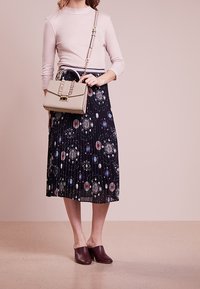 Ljusrosa långärmad topp, mönstrad plisserad svart kjol med färgglada cirkulära mönster, beige handväska och mörkburgunder klackar.