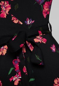 Tissu noir avec un motif floral rose, violet et vert noué en un nœud papillon autour de la taille d'un vêtement.