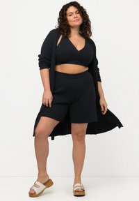 Navy ribbed lounge set, joka koostuu lyhyestä topista, korkeavyötäröisistä shortseista ja pitkästä neuletakista. Asusteena ovat valkoiset sandaalit.