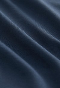 Tessuto blu navy con texture morbida e liscia, con una lieve lucentezza e fine costina, che si drappeggia in onde delicate.