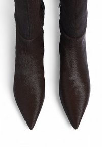 Botines de tobillo marrones con punta afilada, con una textura lisa y brillante, fabricados en un material suave con un diseño elegante y cierre de cremallera lateral.