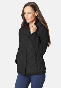 Chaqueta acolchada negra con capucha, que presenta bolsillos laterales y una mezcla de tela suave y texturizada. Cierre frontal con cremallera y herrajes decorativos.