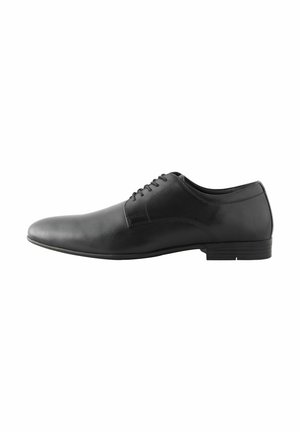 Zapato de vestir de piel negra con superficie lisa, puntera redondeada, tacón bajo y diseño de cordones con seis ojales. Detalle de costura mínima.