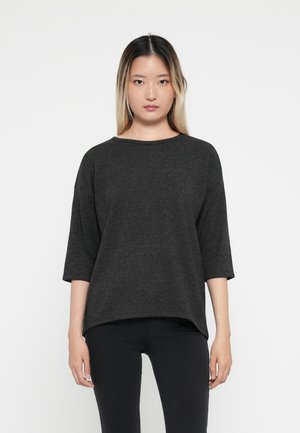 Haut surdimensionné noir foncé avec des manches trois-quarts, encolure ronde, texture douce. Associé à un pantalon noir ajusté pour un look décontracté.