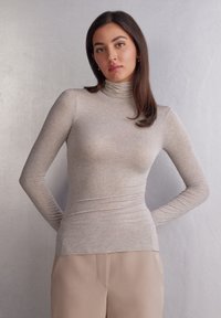 Béžový rolák vyrobený z lehké, ribbené látky. Dlouhé rukávy s přiléhavým střihem, spárované s béžovými kalhotami s vysokým pasem.