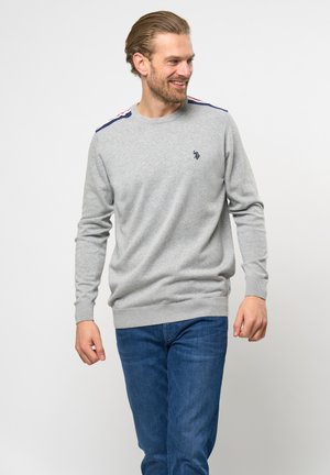 Grauer Strickpullover mit langen Ärmeln, gerippten Bündchen und Saum, mit marineblauen und roten Streifen auf den Schultern. Kleines Logo auf der Brust.