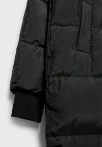 Sort pufferjakke med detalje, der har en tekstureret overflade, elastiske manchetter og en patchlomme på overarmen. Glat, skinnende stof.