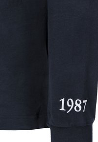 Marinblå långärmad t-shirt i mjukt bomullstyg, figursydd design och vitt broderat "1987" på vänster ärm.