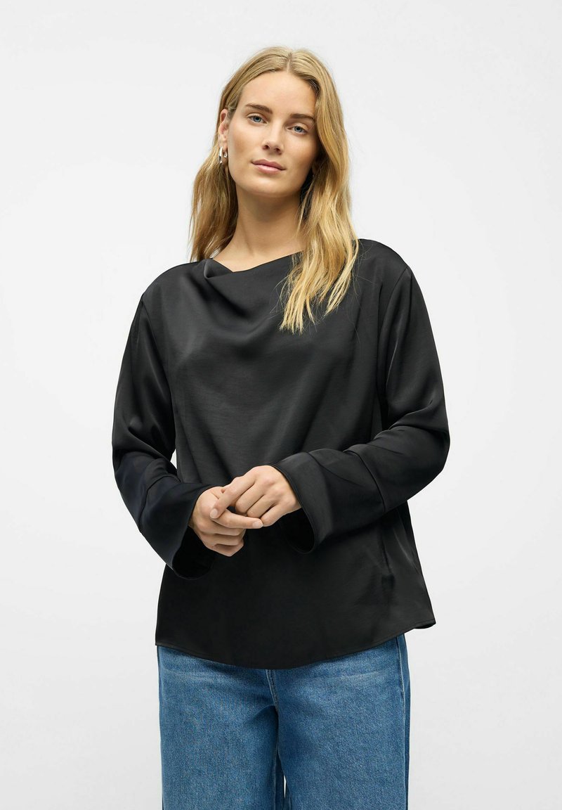 Schwarz, langärmeliges Shirt mit einem Schalkragen und weiten Manschetten. Glatte Textur mit einer lockeren Passform, kombiniert mit hellblauen Jeans.
