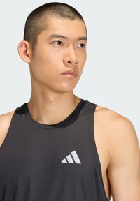 Black athletic tank top made of smooth fabric, featuring a rounded neckline and a white logo on the left chest area. Tight fit.