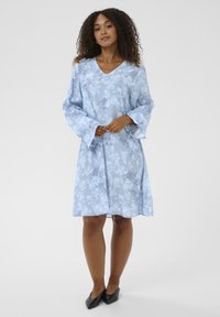 Hellblaues Blumenkleid mit V-Ausschnitt und Glockenärmeln. Hergestellt aus weichem Stoff, mit einem dezenten Blumenmuster und einer lockeren Silhouette.