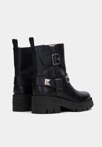 Botas negras de cuero hasta el tobillo con un acabado texturizado, adornos de remaches, hebilla ajustable y suela de goma gruesa y estriada.