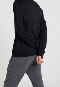 Black sweatshirt with long sleeves, round neckline, and ribbed cuffs, paired with gray tapered pants featuring a subtle texture.