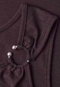 Gros plan sur un tissu violet foncé avec deux boucles rassemblées reliées par des fermoirs à boules en métal argenté.