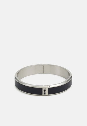 Bracciale in metallo argentato con una striscia in pelle nera. Presenta un design liscio e arrotondato e il logo "BOSS" su un accentuazione metallica.