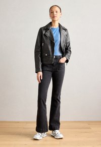 Black leather biker jacket over a blue ribbed top, paired with flared black jeans and white sneakers. The outfit features a sleek design.