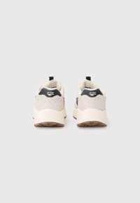Beige og mørkegrå treningssko med en teksturert overdel, polstret såle og liten svart hæltab. Har logo på hælen.