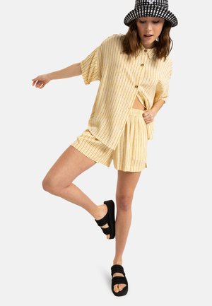 Yellow striped short-sleeve shirt and matching shorts, made of lightweight fabric. Black sandals with two wide straps. Black and white checkered hat.