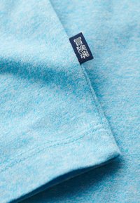 T-shirt di cotone azzurro chiaro con una texture morbida, caratterizzata da un'etichetta blu scuro con testo bianco cucita sul lato.
