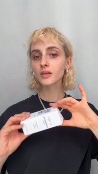 TIRTIR Niacinamide 20% serum i en hvit rektangulær boks med lilla tekst og strekkoder holdt i én hånd, mot en grå bakgrunn.