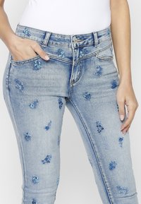 Ljusblå denimjeans med blommönster broderat i olika nyanser av blått, med en medelhög midja, fem fickor och en smal passform.