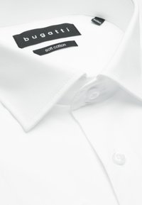 Kragen eines weißen Hemdes mit sichtbarem Bugatti-Logo und Etiketten aus weichem Baumwollstoff, das einen Knopf an der Knopfleiste zeigt.