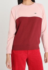 Rosa und rote farbige Block-Sweatshirt mit geripptem Muster, runder Ausschnitt und Raglanärmeln. Kleines Lacoste-Logo auf der Brust.