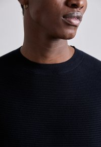 Navy-blaues, geripptes Strickpullover mit Rundhalsausschnitt und strukturiertem Stoff, der ein dezentes Muster und weiches, warmes Material betont.