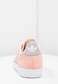 Růžové semišové tenisky s šedým patním dílem a bílým logem. Na straně obsahují tři šedé pruhy a mají strukturovanou bílou podrážku.